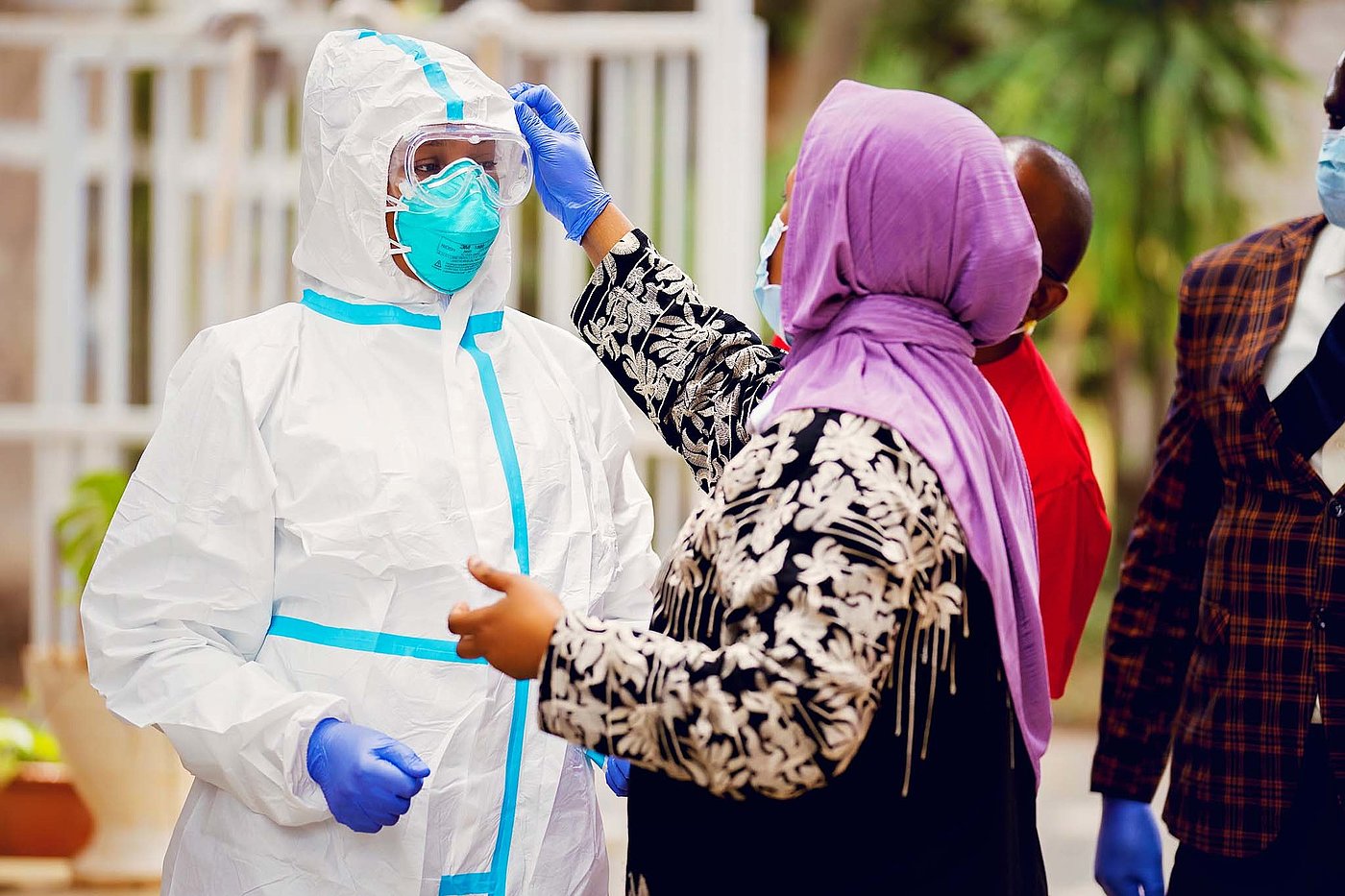 Photo: A woman uses her hand to check the head area of a protective suit worn by the person standing opposite her.