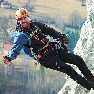 Photo: A person roped up on a cliff face. He is wearing a climbing harness and a helmet, and giving a thumbs-up.