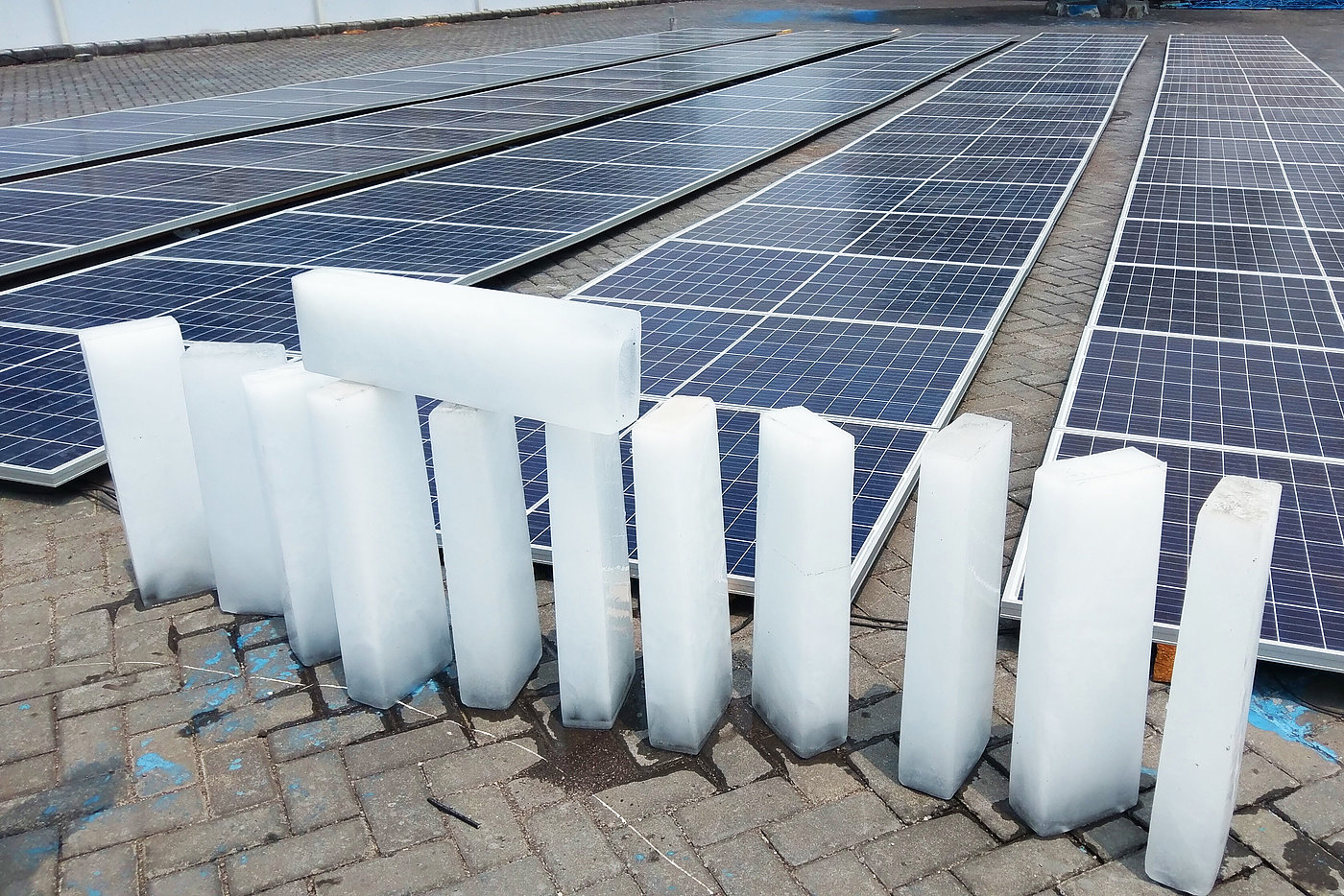 Photo: A yard with many solar panels on the floor. Small blocks of ice are lined up at the front.