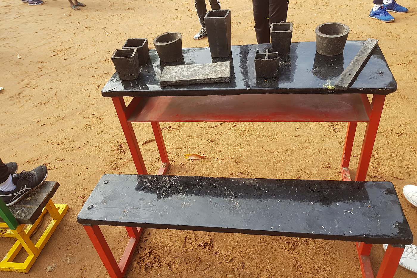 Photo: A number of clay vessels stand on a table outside. A bench stands in front of the table.