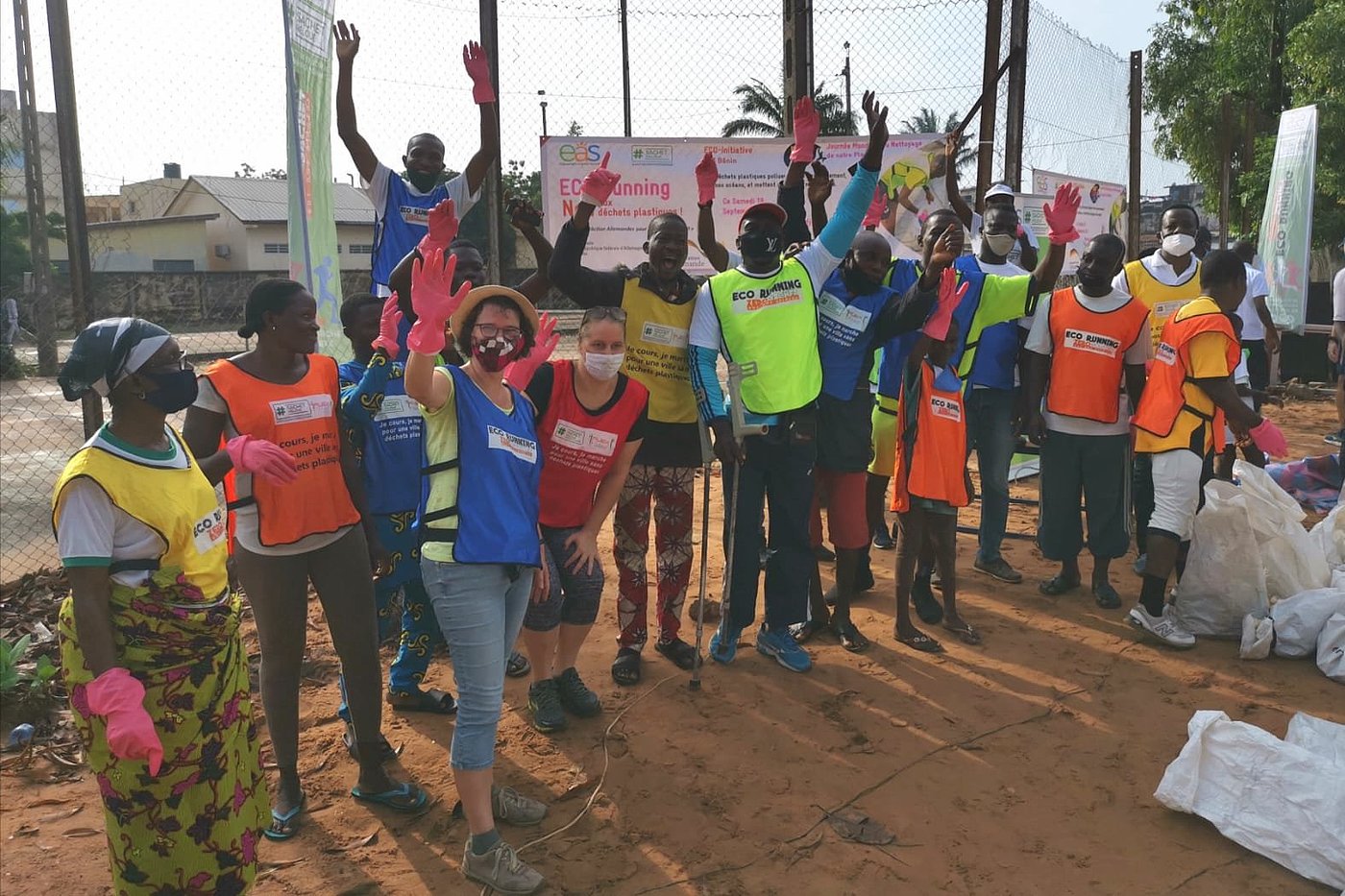 Photo: People wearing face coverings pose for the camera in front of a sign that says ‘ECO-running - Non aux déchets plastiques!’. They are wearing different coloured warning vests.