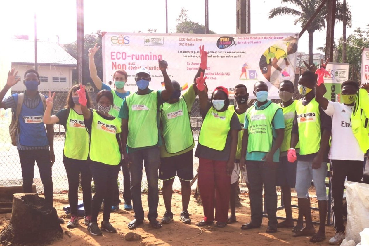 Photo: People wearing face coverings pose for the camera in front of a sign that says ‘ECO-running - Non aux déchets plastiques!’. Most are wearing greenish yellow warning vests.