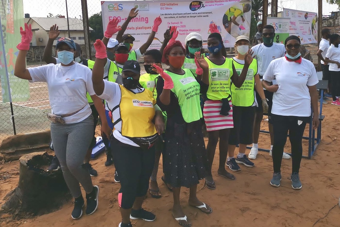 Photo: People wearing face coverings pose for the camera in front of a sign that says ‘ECO-running - Non aux déchets plastiques!’. Most are wearing greenish yellow warning vests.