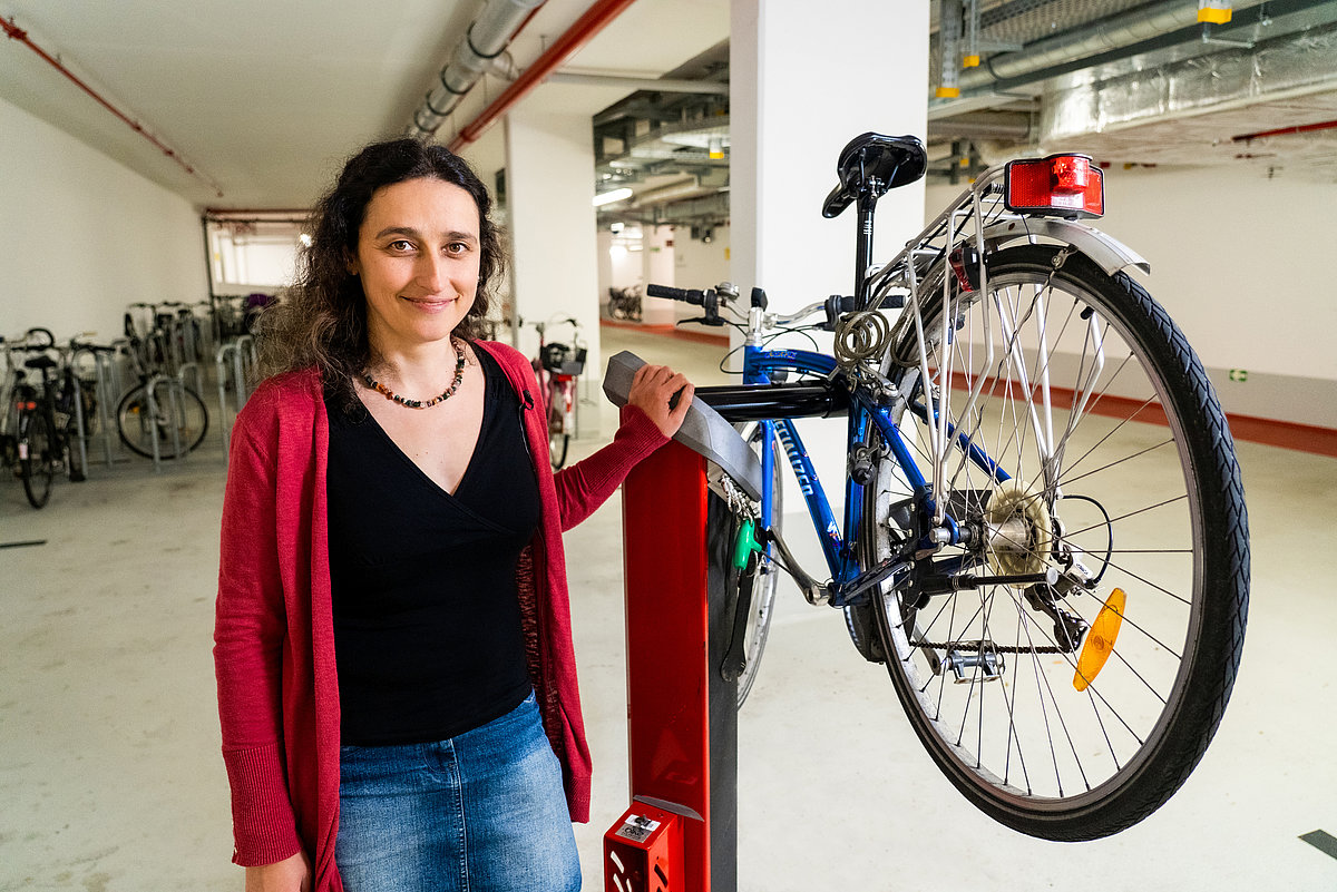 Photo: A woman stands in a large hall next to a bicycle lift with a bicycle on it.