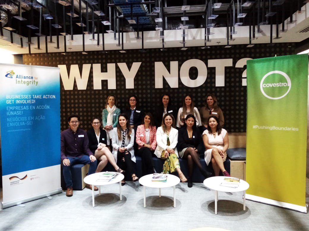 Photo: Several people sit in two rows in front of a wall bearing the words ‘Why not?’ Roll-up banners can be seen to their right and left.