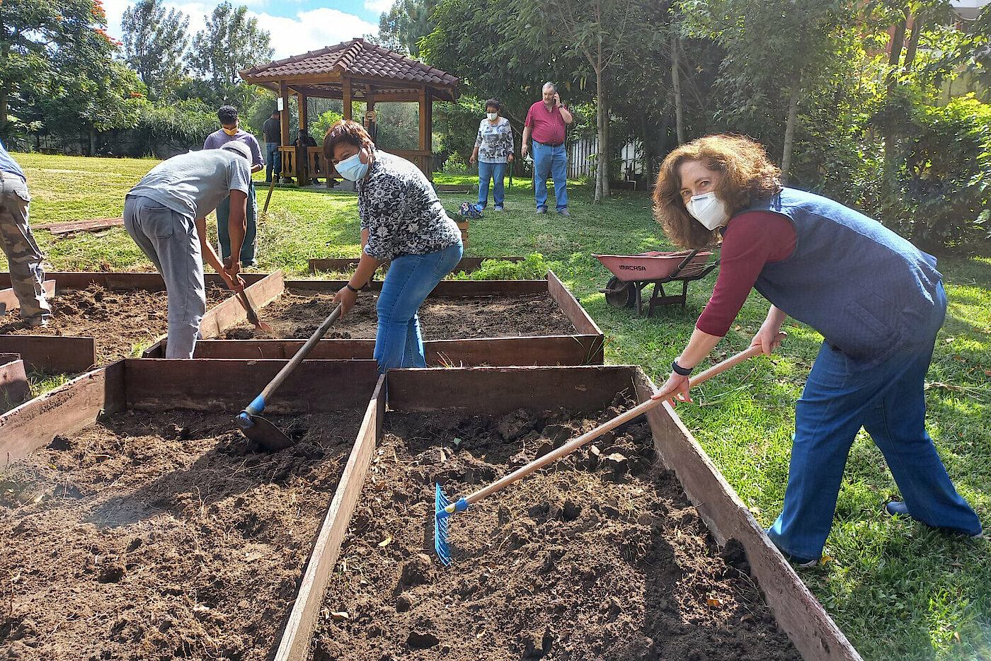 Photo: Several people using hoes and rakes in wooden plant beds. 