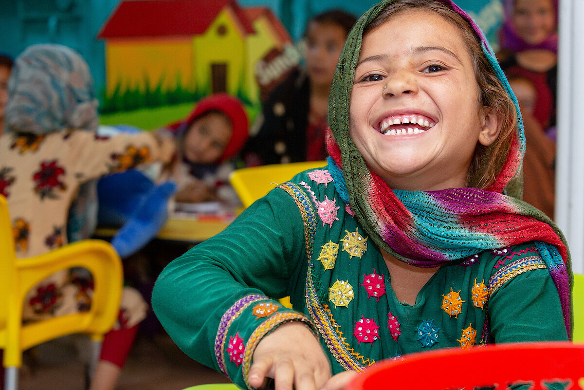 Photo: A girl with a colourful dress and scarf smiling at the camera.