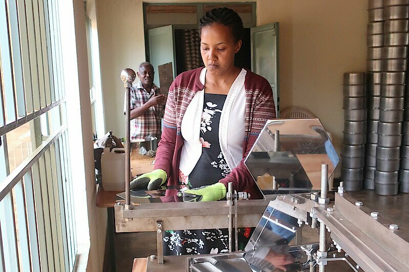 Photo: A woman wearing gloves standing at a machine holding a mirror tile.
