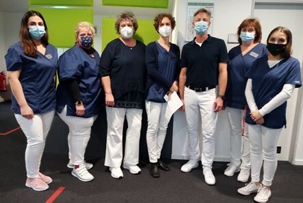 Foto: Sechs Frauen und ein Mann in weißen Hosen, blauen Oberteilen und mit Mundschutz stehen nebeneinander.