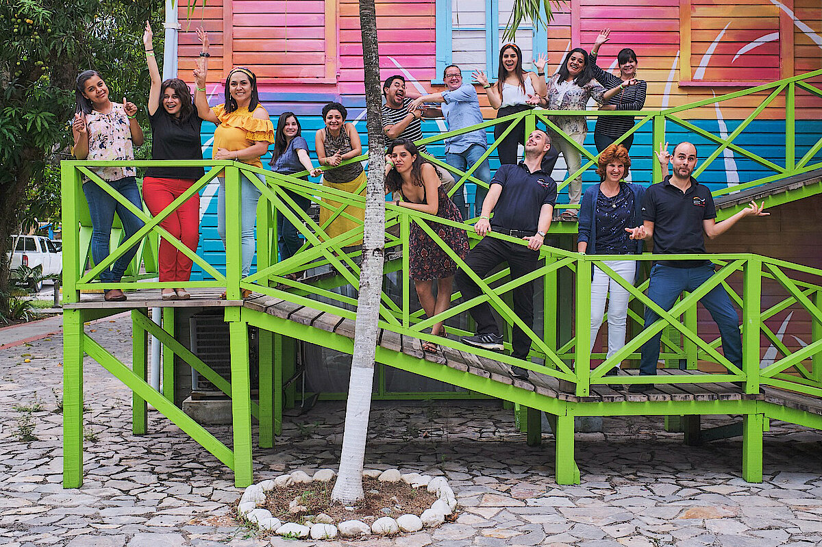 Photo: Several people standing on an access slope with green railings in front of a colourful building.