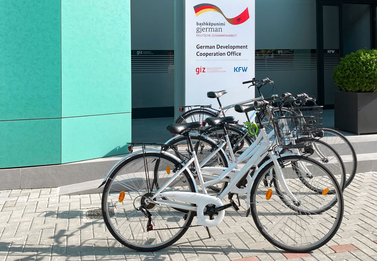 Foto: Mehrere Fahrräder stehen nebeneinander vor einem Gebäude mit einem Schild: „German Development Cooperation Office“.
