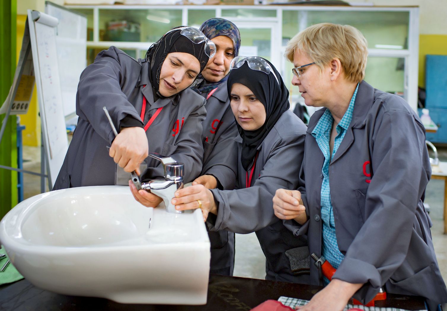 Photo: Four women in work coats stand around a sink. One woman is screwing on the tap, another woman is holding it.