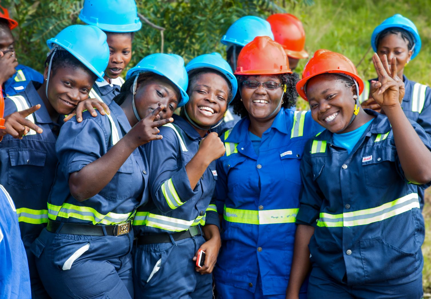 Group photo: Several women in work clothes and helmets are smiling.