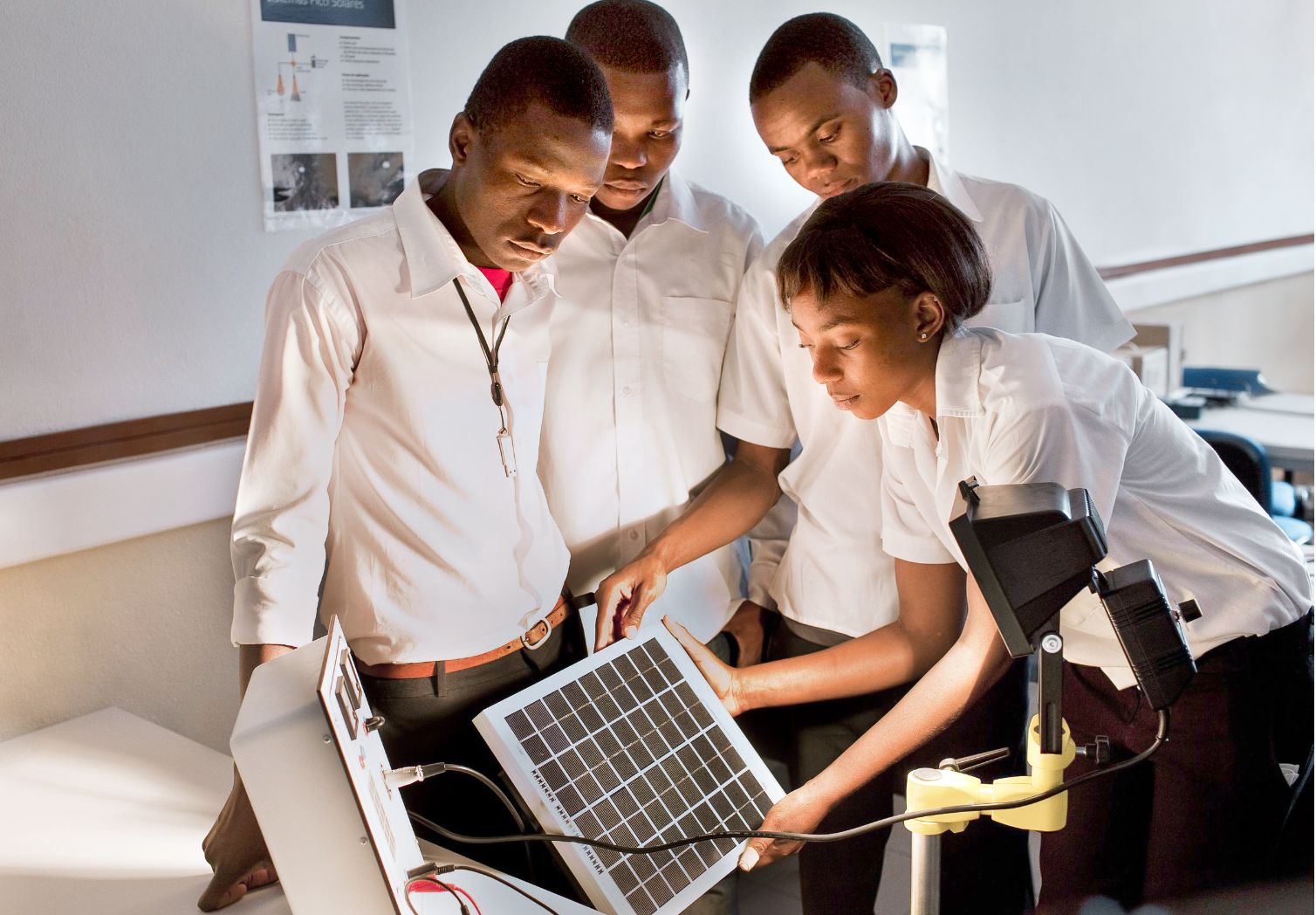 Photo: Four people standing around a solar panel illuminated by a lamp.