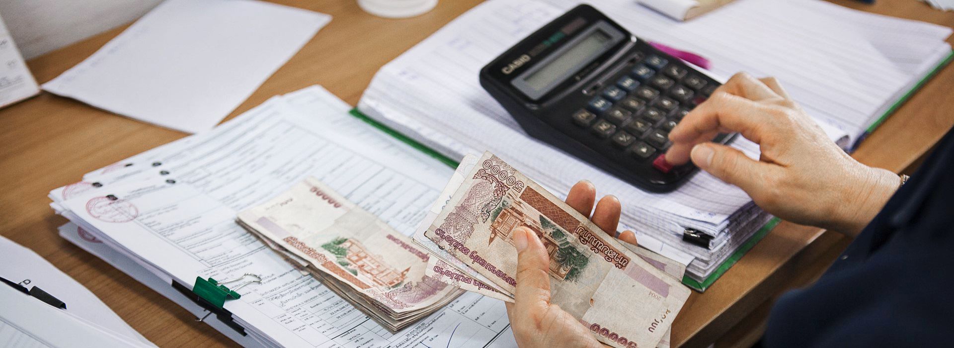 Photo: Documents, banknotes and a hand entering figures on a calculator.