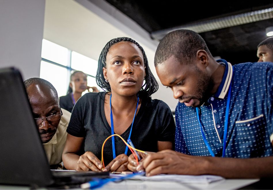 Photo: Several people working on something together, with cables and a laptop in front of them.