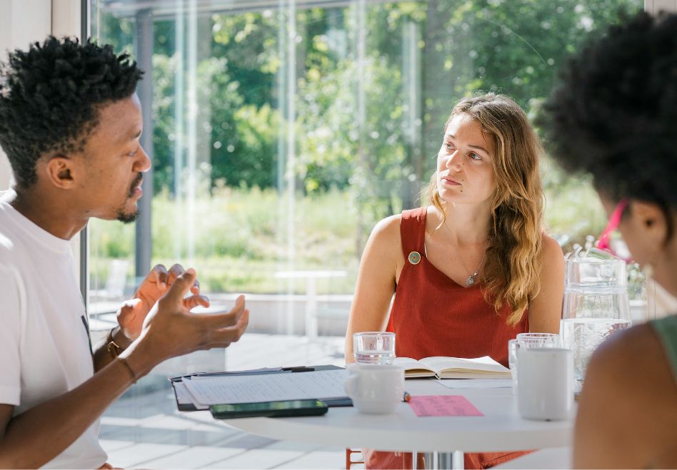 Photo: Three people having a conversation around a table.