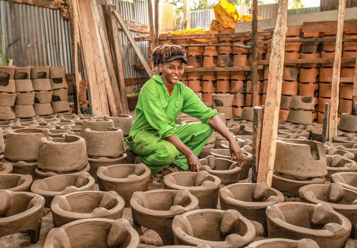 Photo: A woman crouching among many clay pots.