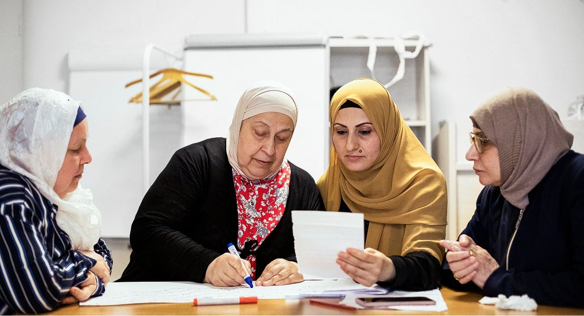 Photo: Four women wearing headscarves sitting around a table and learning together.