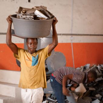 Photo: A young man carrying a plastic basin containing plastic waste on his head.