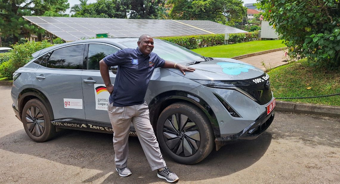 Photo: A man leaning against an electric SUV looks towards the camera with a friendly expression.