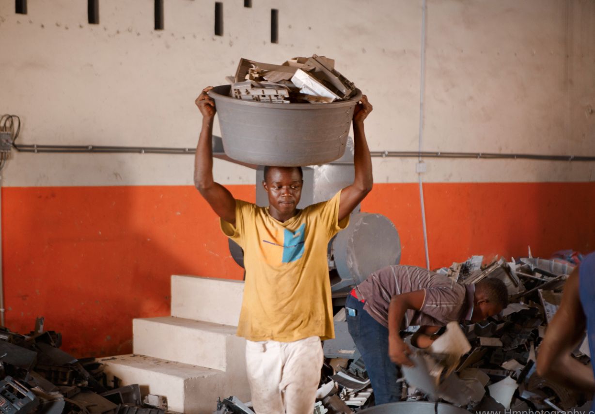 Photo: A young man carrying a plastic basin containing plastic waste on his head.