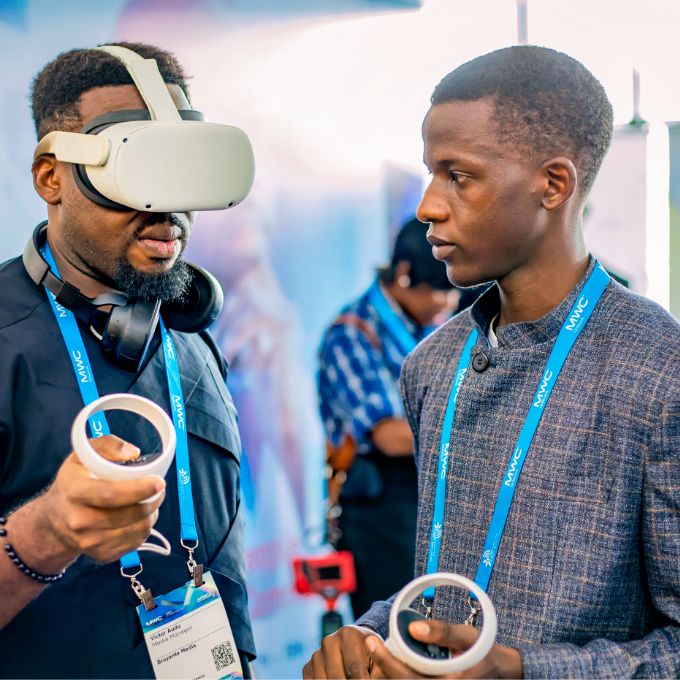 Photo: Two men standing face-to-face. The man on the left is wearing a VR headset.