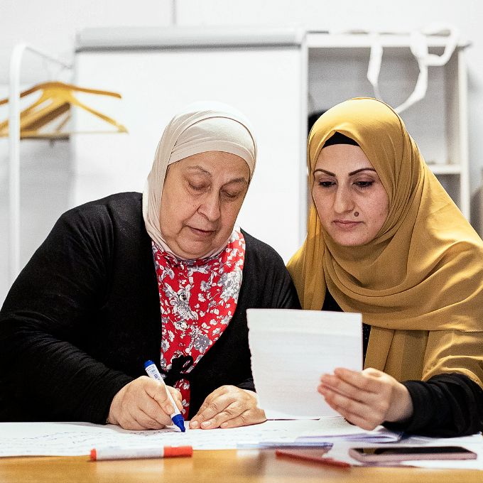 Photo: Two women wearing headscarves sitting around a table and learning together.