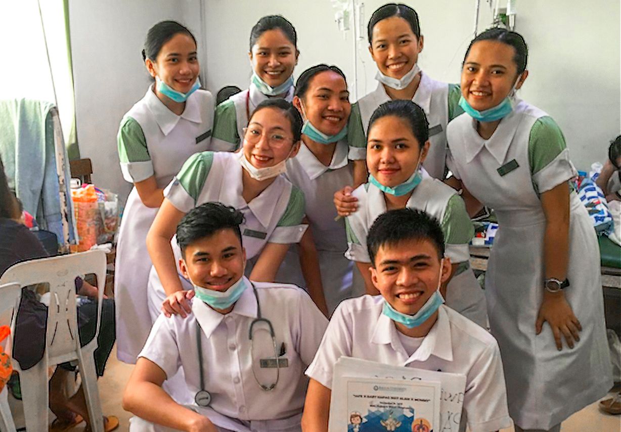 Photo: Seven young women and two young men wearing medical scrubs pose for a group photo.