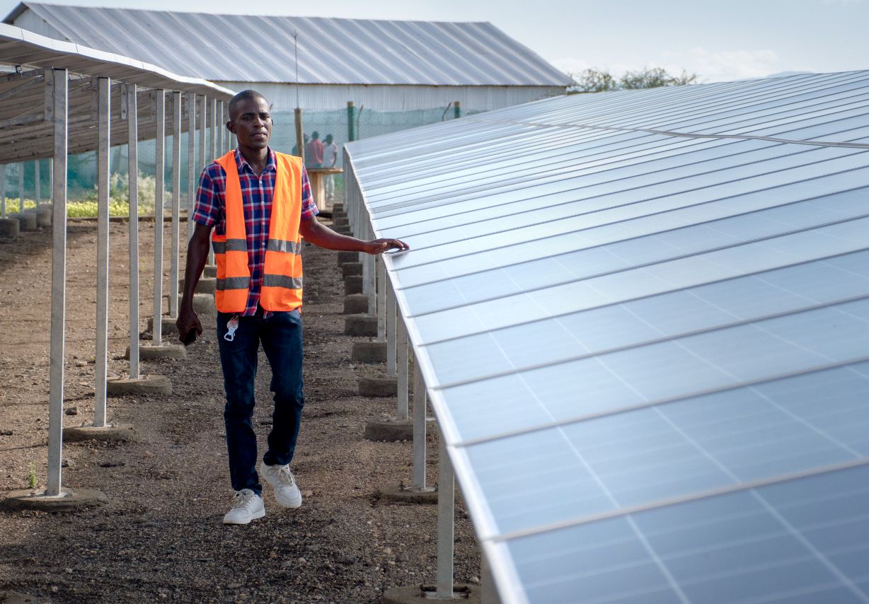 Photo: A man in a hi-vis jacket walking past a row of solar panels.