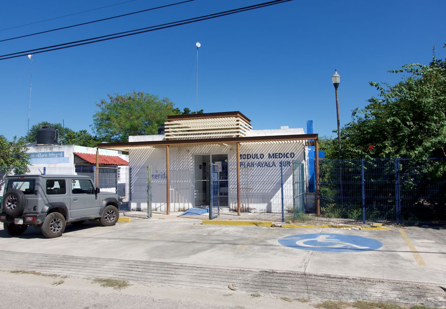 Photo: A car parked on a concrete surface in front of a small building behind a fence.