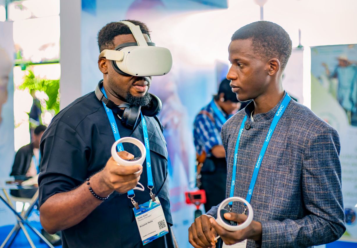 Photo: Two men standing face-to-face. The man on the left is wearing a VR headset.