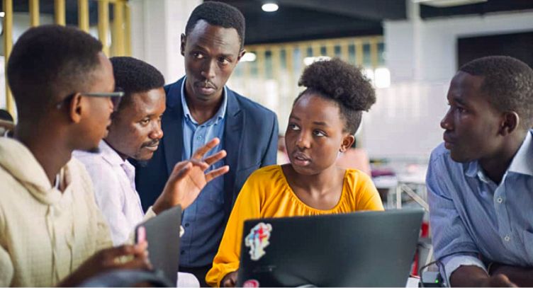 Photo: Five people in discussion gather around a laptop.