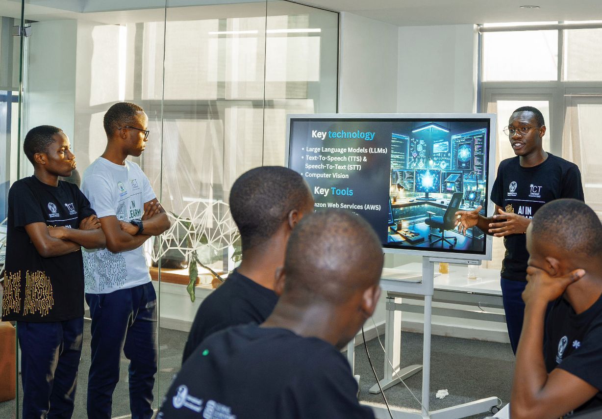 Photo: A man stands next to a large screen and explains something. Several people are listening.