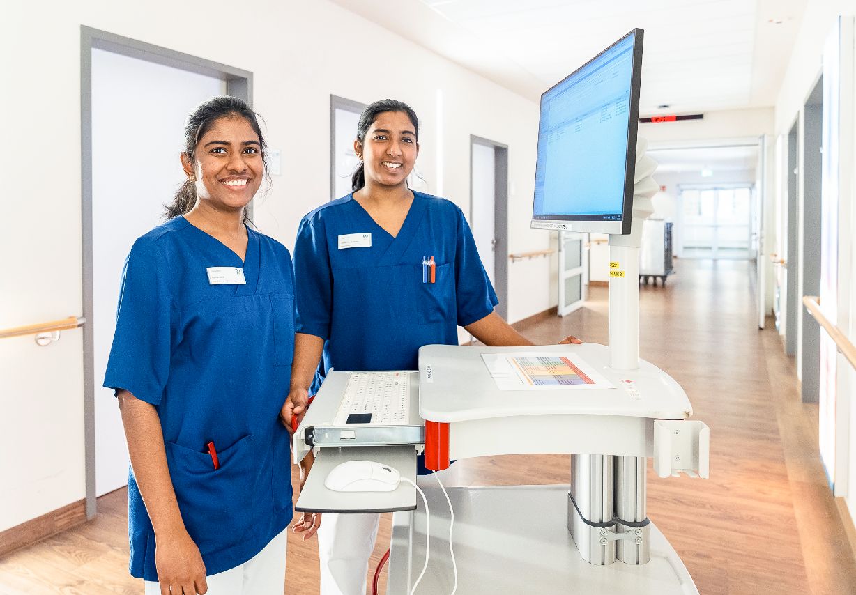 Photo: Two young women in dark blue scrubs standing in a hospital corridor next to a monitor. &copy; GIZ, Photo: Tristan Vostry