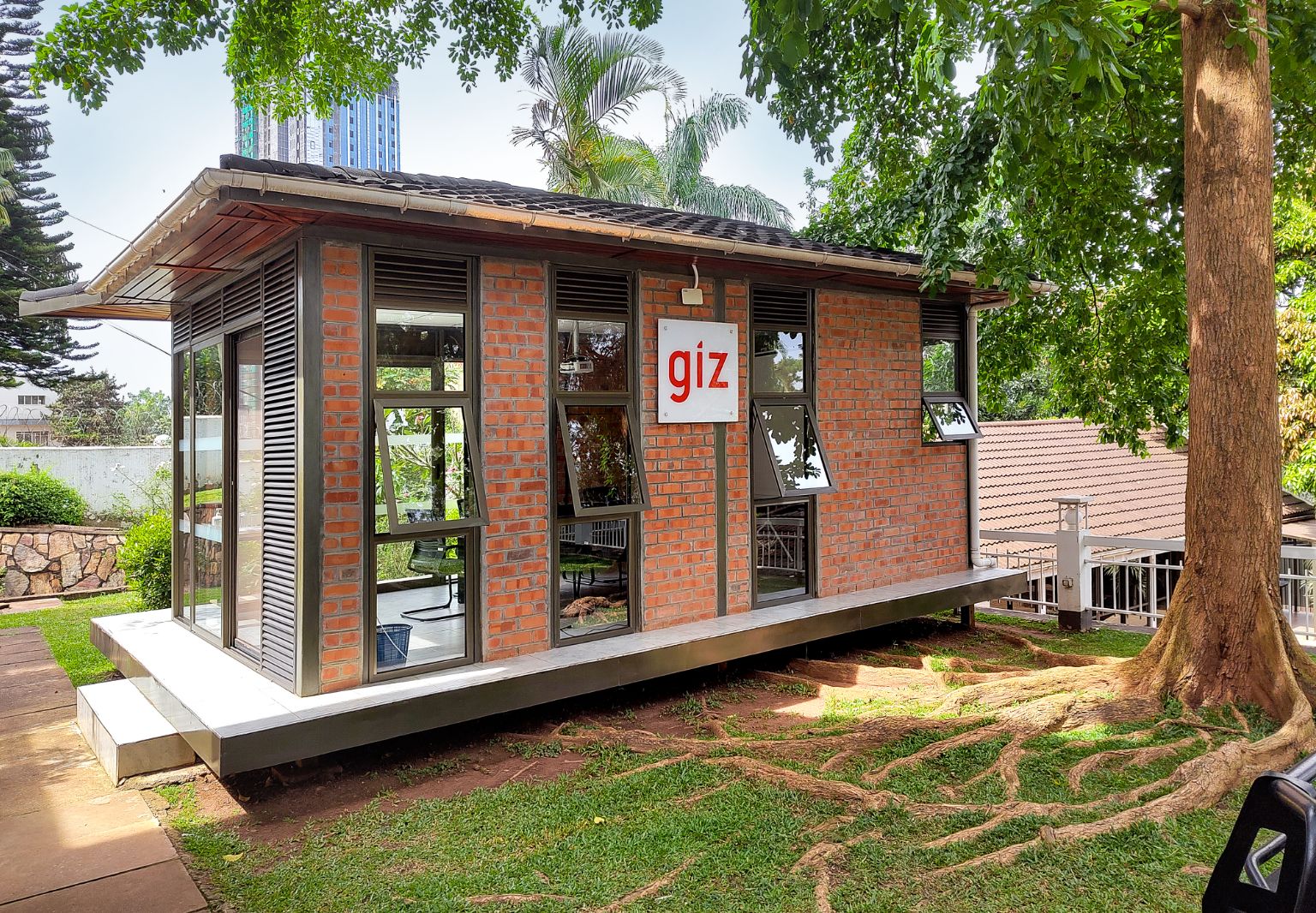 Photo: A small building with a GIZ logo, elevated slightly on stilts over tree roots. A tree stands next to it on the right.