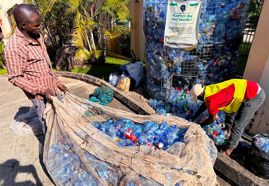 Photo: Two men emptying a container filled with plastic bottles.