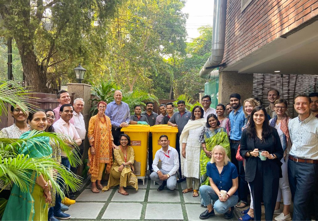 Photo: Group photo of around thirty people posing around two yellow rubbish bins.