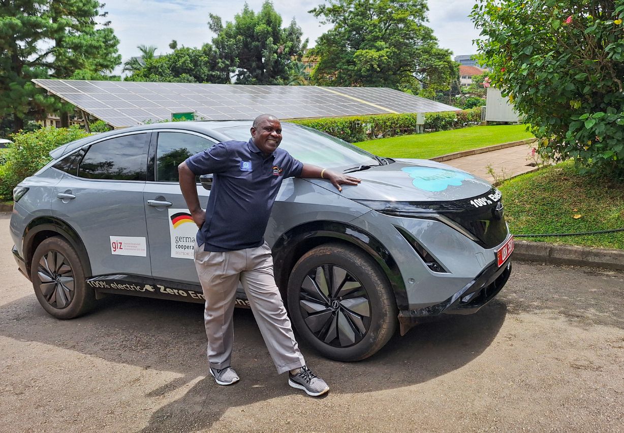 Photo: A man leaning against an electric SUV looks towards the camera with a friendly expression.