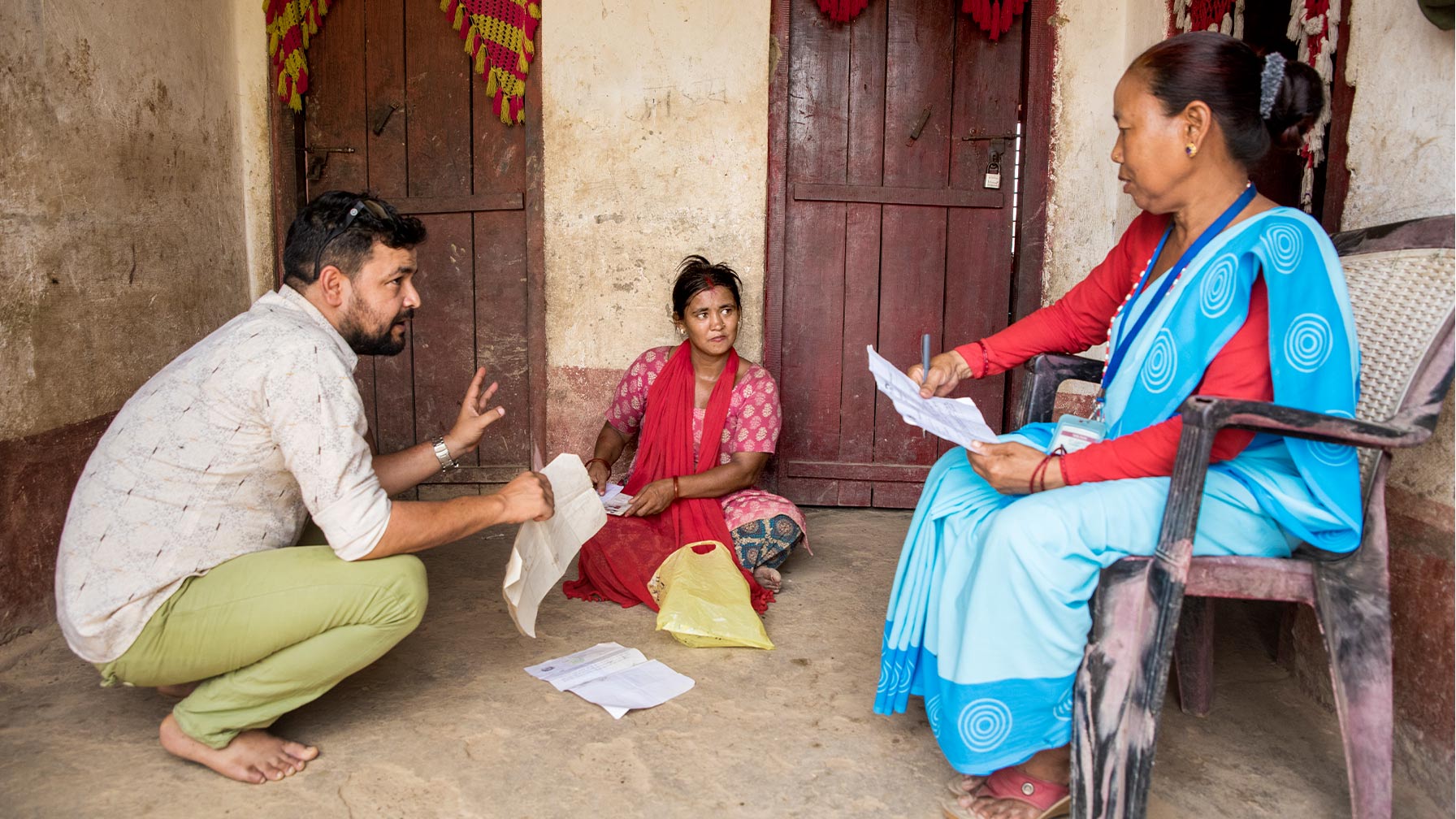 A man and two Nepalese women sitting together, holding documents in their hands and talking intently with one another.