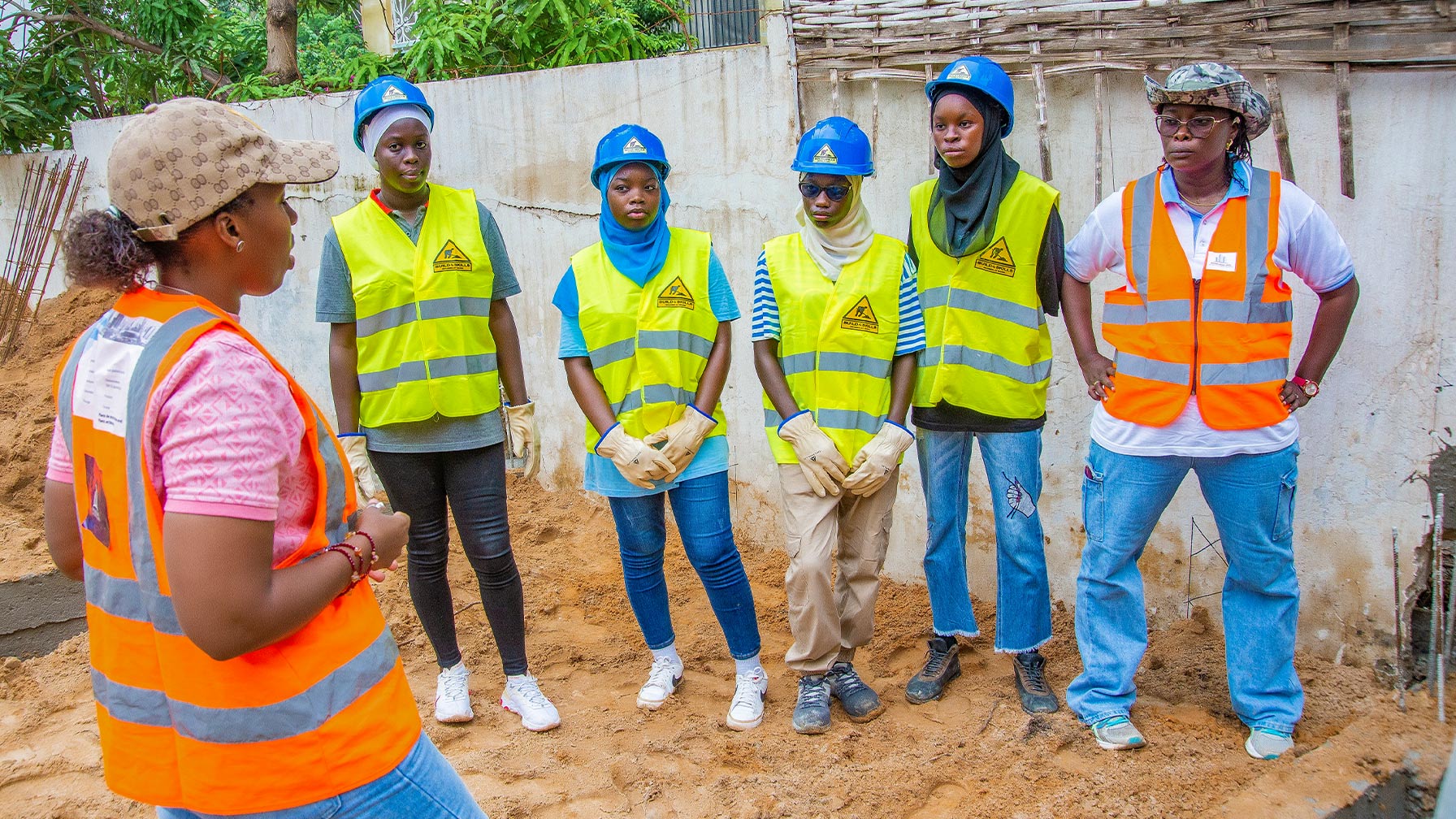 Group photo with Djélia Diagne (in profile on the left) talking to five young women in hard hats and high-visibility vests on a construction site.